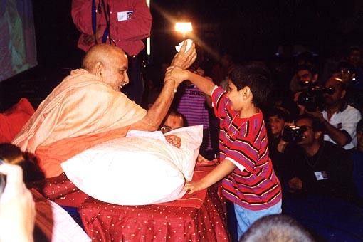 Swamishri entertains boy trying to grab a packet of prasad