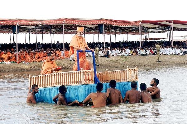 Swamishri is brought to the middle of the river standing on a decorated raft
