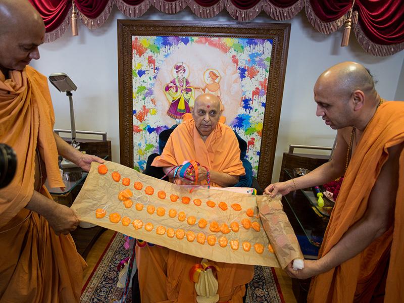  Swamishri is honored with a garland made of traditional sweets