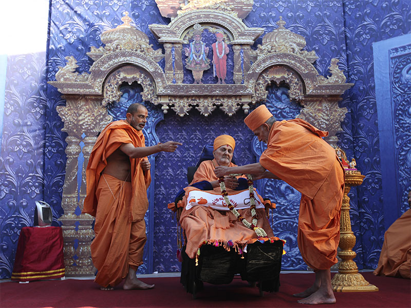 Pujya Keshavjivan Swami (Pujya Mahant Swami) honors Swamishri with a garland