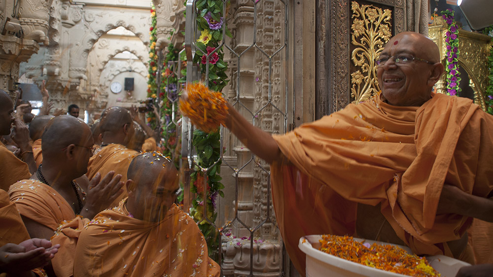Pujya Tyagvallabh Swami and senior sadhus spray sanctified colored water and flowers on sadhus