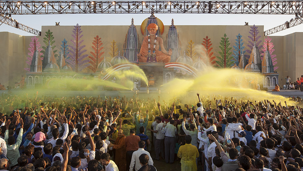 Swamishri showers sanctified colored water on devotees and blesses them