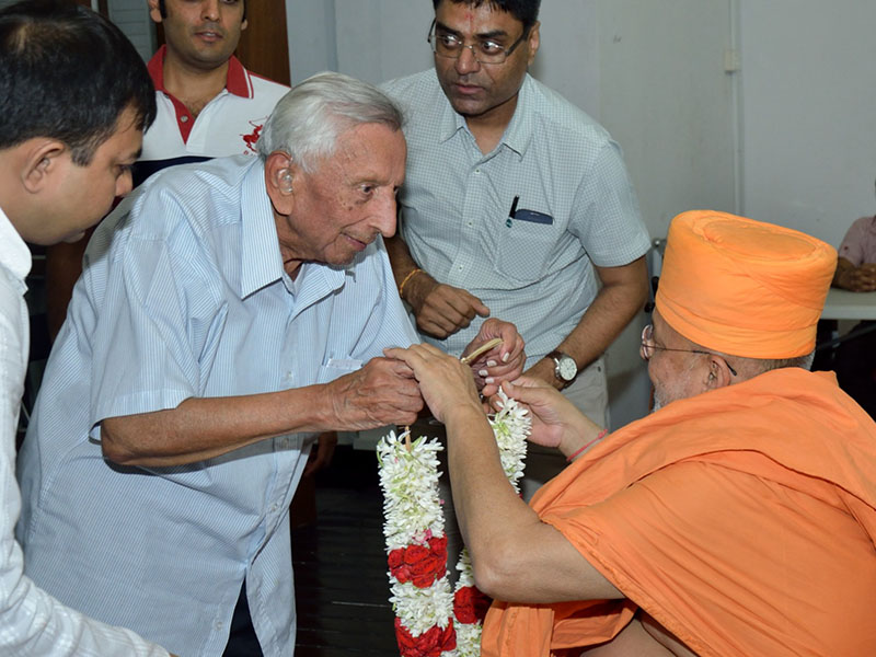 A devotee honors Pujya Ishwarcharan Swami with a garland