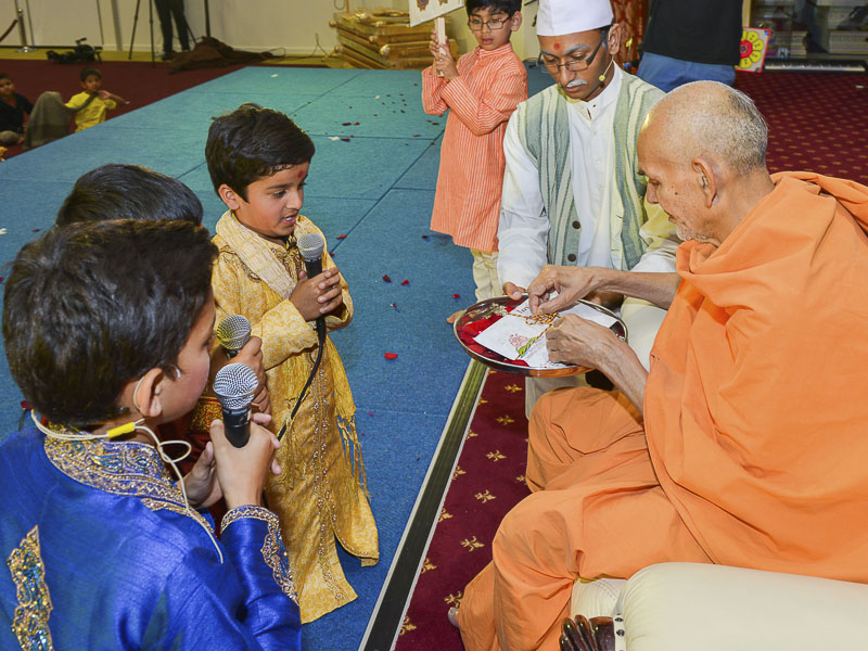 Pujya Mahant Swami inaugurates the Adelaide Mandir Murti Pratishtha invitation card while children recite Sanskrit shlokas